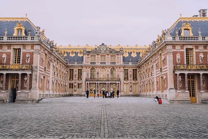 Exterior view of the Château de Versailles with its iconic gardens and ornate facade under a clear sky.