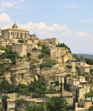 Panoramic view of Gordes village perched on a hill in Provence, with stone houses and lavender fields under a blue sky.