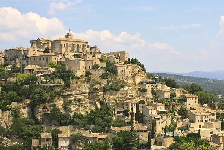 Panoramic view of Gordes village perched on a hill in Provence, with stone houses and lavender fields under a blue sky.