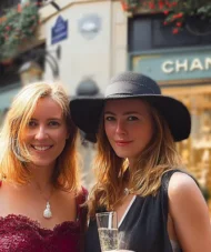 Two women in Paris, one holding a champagne glass, in front of a Chanel boutique — Paris Fashion Tour.