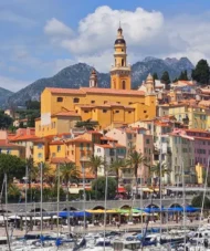 Colorful houses of Menton overlooking the harbor with boats and mountains in the background, French Riviera, France.
