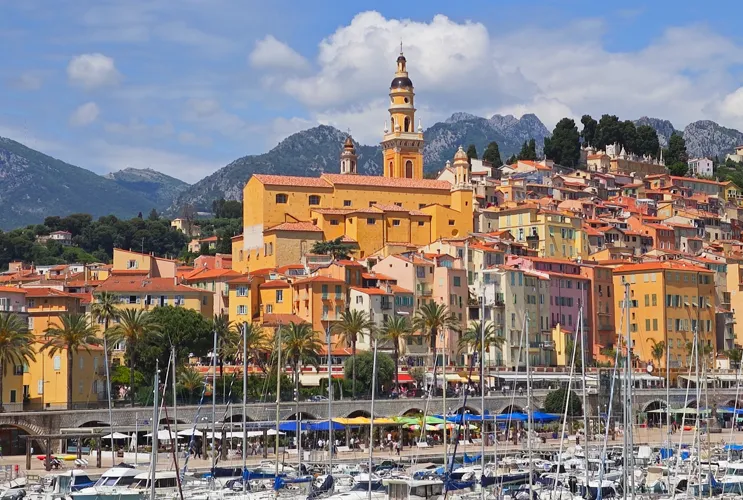 Colorful houses of Menton overlooking the harbor with boats and mountains in the background, French Riviera, France.