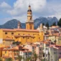 Colorful houses of Menton overlooking the harbor with boats and mountains in the background, French Riviera, France.